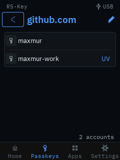 The trusted display’s per-service passkey detail for github.com: a back chevron and a pencil rename affordance beside the title, two account rows (maxmur, and maxmur-work marked UV), and a “2 accounts” footer